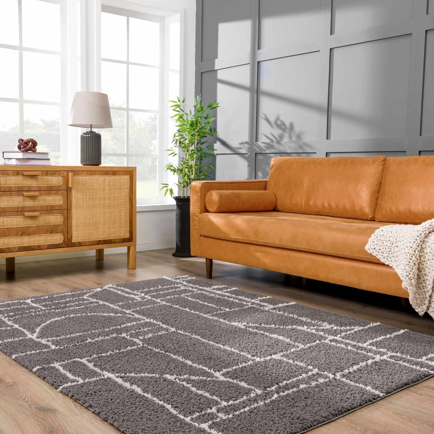 Living room scene with a tan leather sofa and the gray geometric Andia Charcoal Area Rug. Roomscene-Rectangle