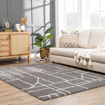 Living room scene with a gray and white geometric Andia Charcoal Area Rug, sofa, and wood cabinet. Roomscene-Rectangle