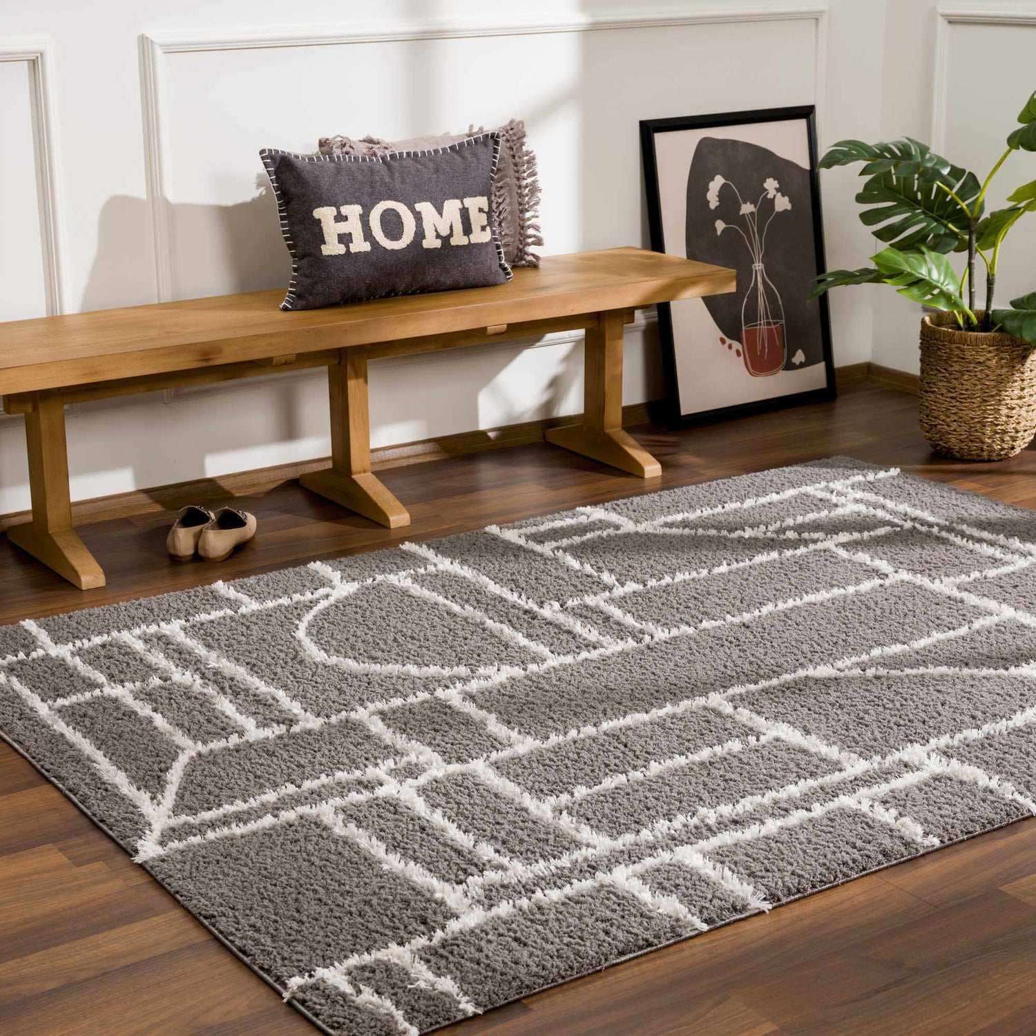 Entryway scene with geometric Andia Charcoal Area Rug, wood bench, pillow, art, plant, and wood floors. Roomscene-Rectangle