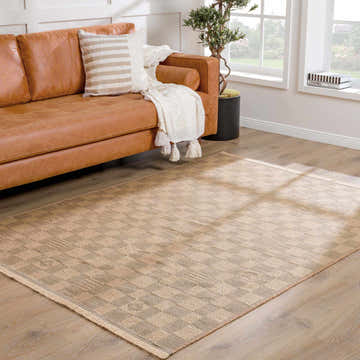 Living room scene with a beige Nairi Checkered Washable Jute Rug, brown leather sofa, and natural light from a window. Roomscene-Rectangle