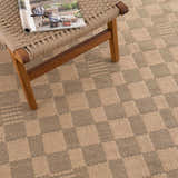 Close-up of the beige and black checkered Nairi Washable Jute Rug, showing the texture and pattern with a chair on top. Styleshot