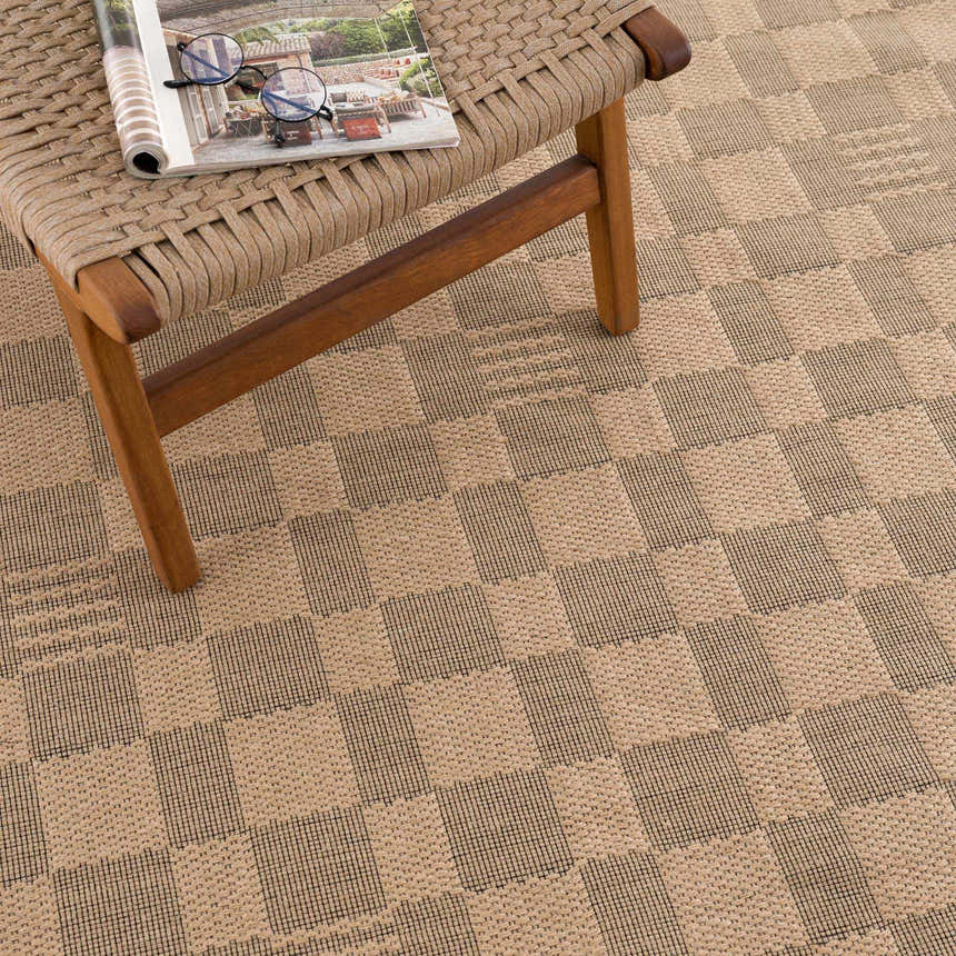 Close-up of the beige and black checkered Nairi Washable Jute Rug, showing the texture and pattern with a chair on top. Styleshot
