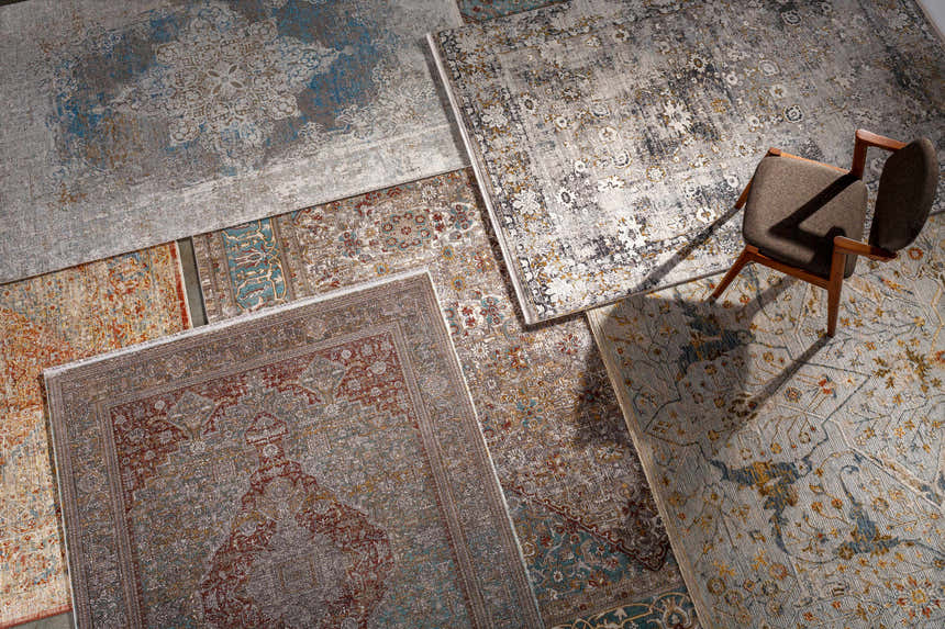 Overhead view of assorted Candiis Luxe Performance Rugs in various colors and patterns, with a chair. Styleshot