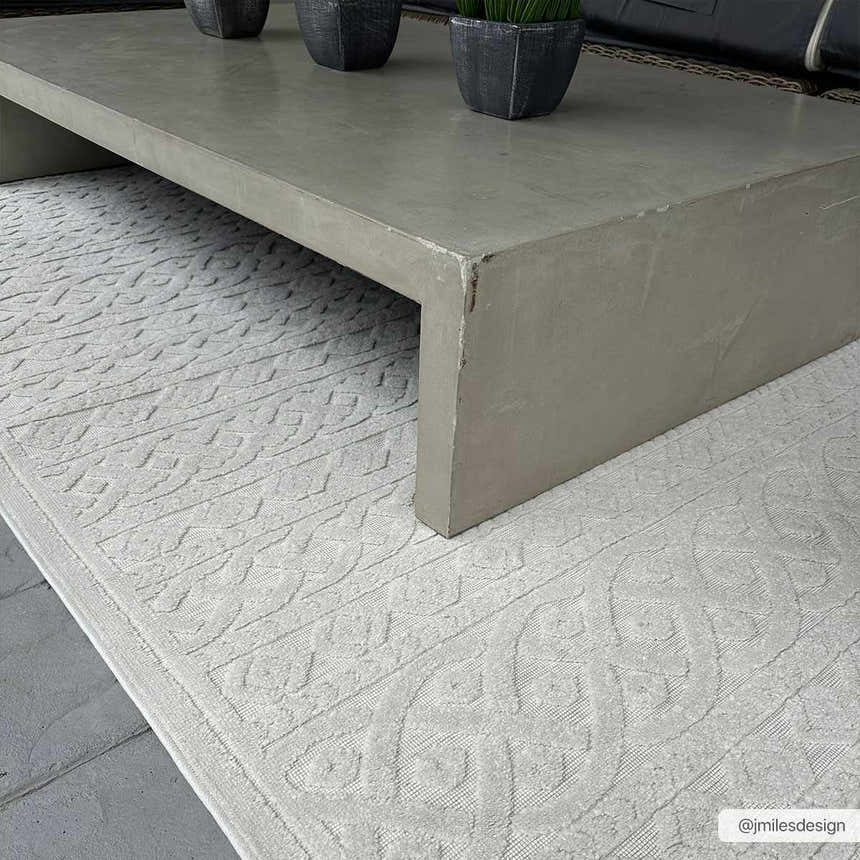 Close-up of the cream Maribyrnong 3D Outdoor Area Rug featuring a raised, geometric pattern under a gray concrete coffee table. Roomscene-Rectangle