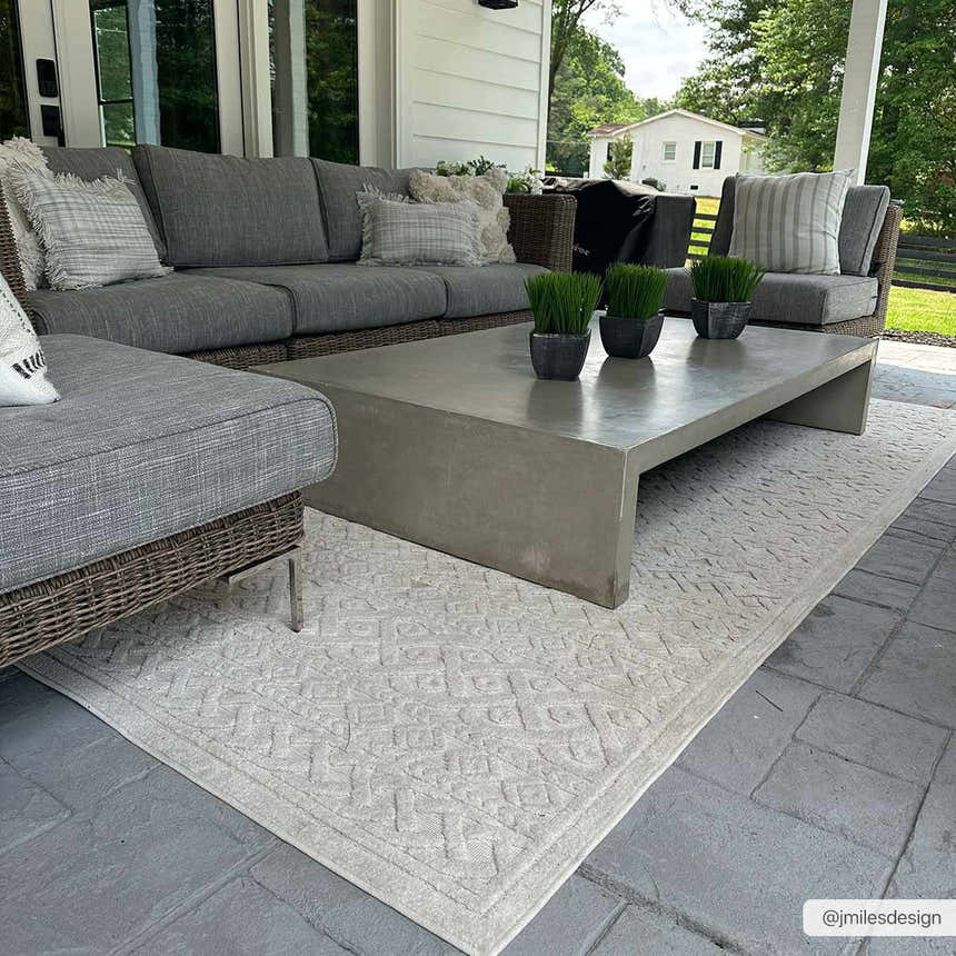 Cozy patio with gray wicker sofa, concrete table, and cream Maribyrnong 3D Outdoor Area Rug. Roomscene-Rectangle