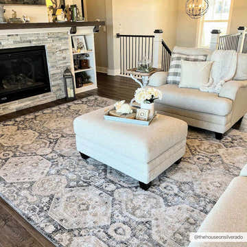 Living room scene with a beige Minoa Area Rug, ottoman, and chair near a stone fireplace. Roomscene-Rectangle