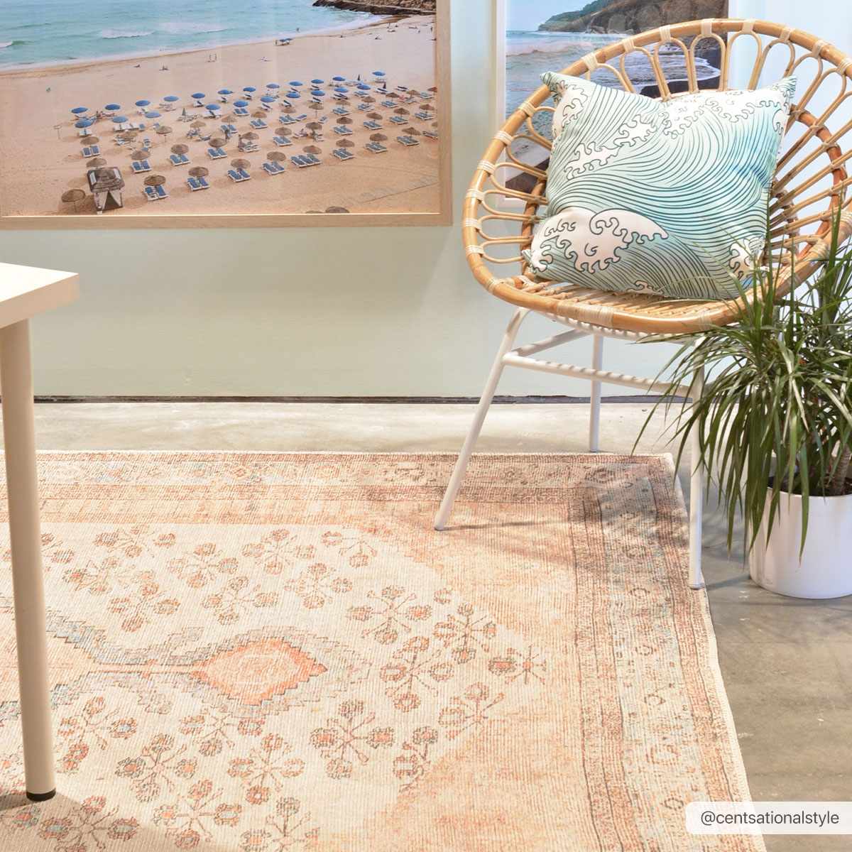 Styled room featuring the Moora Washable Area Rug in blush and beige, with a rattan chair and beachy artwork. Roomscene-Rectangle