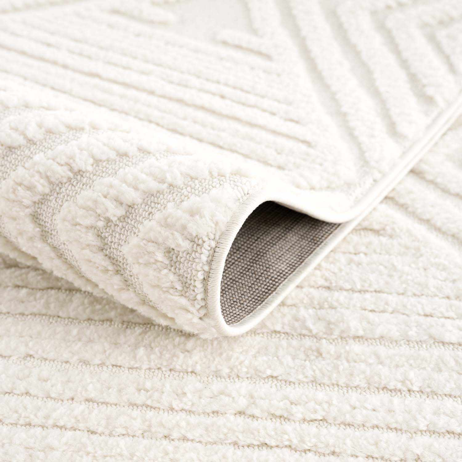 Close-up of the bone-colored Manyas 3D Area Rug showing its geometric pattern, soft texture, and bound edge. Fold