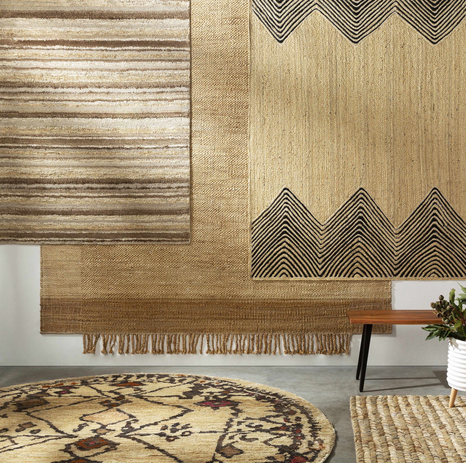 Greenbackvile Area Rug display: Cream, beige, and brown jute and wool rugs with stripes and geometric patterns on a white wall. Styleshot