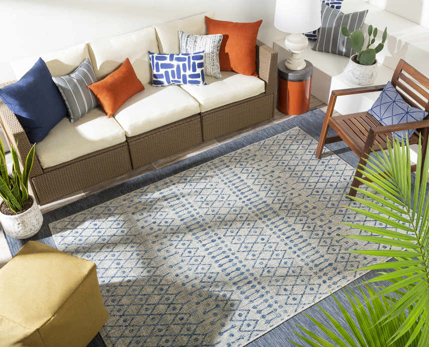 Bohemian patio design with a Newbern Outdoor Rug, wicker sofa, and blue and orange pillows. Styleshot