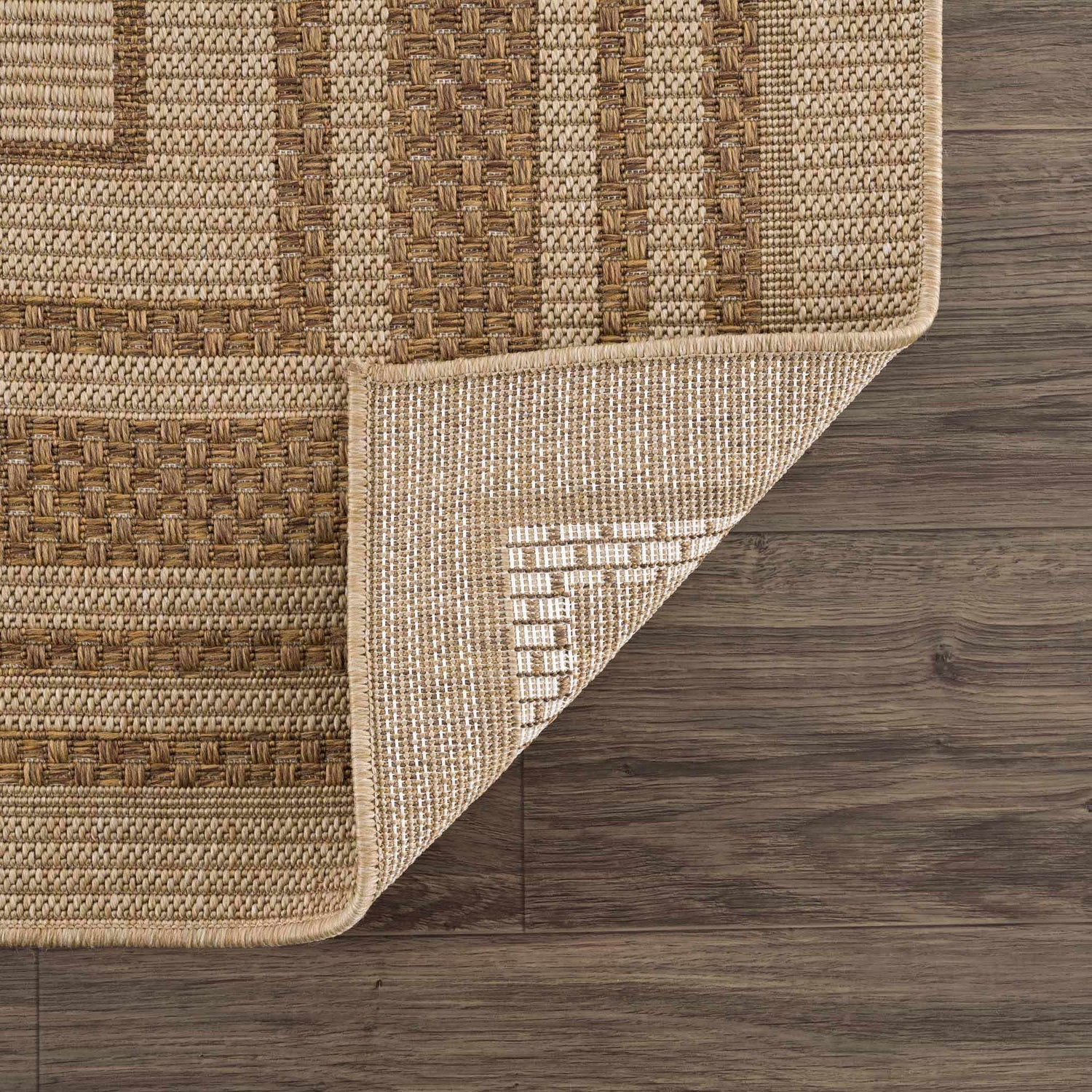 Close-up of the Isoko Bordered Faux Jute Rug showing the camel and brown textured weave and the rug's backing. Fold