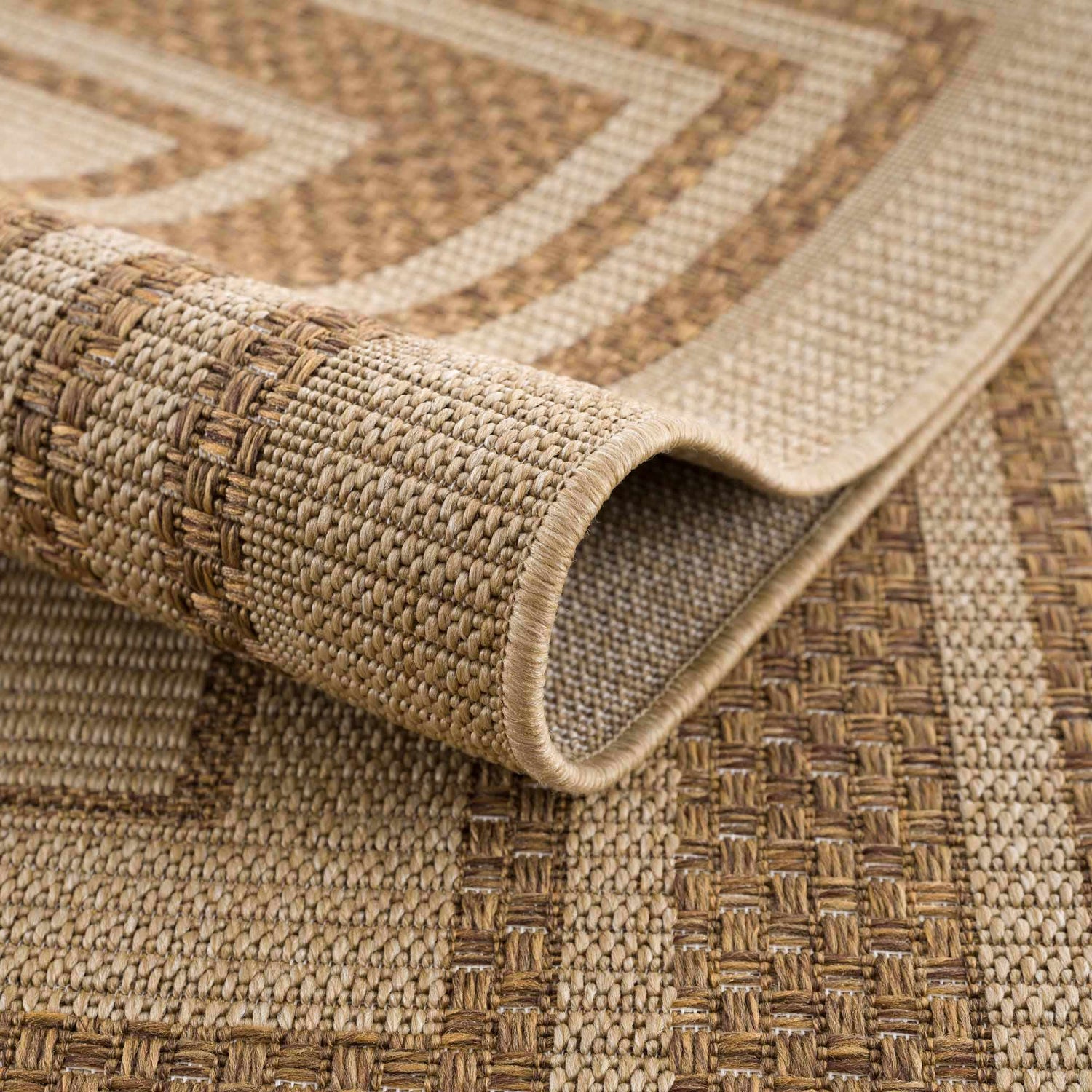 Close-up of the Isoko Bordered Faux Jute Rug. The rug features a textured weave and a geometric border pattern in camel and brown tones. Fold