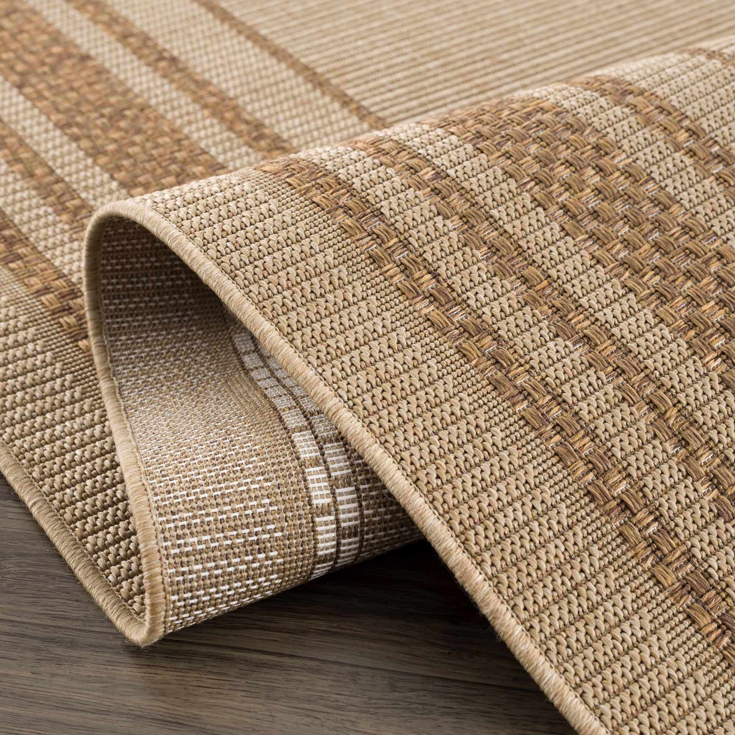 Close-up of the Isoko Bordered Faux Jute Rug showing camel and brown tones, woven texture, and bordered edge. Fold