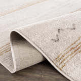 Close-up of the Deja Cream & Gold Area Rug, showing its soft pile, cream color, gold accents, and durable machine-woven construction. Fold