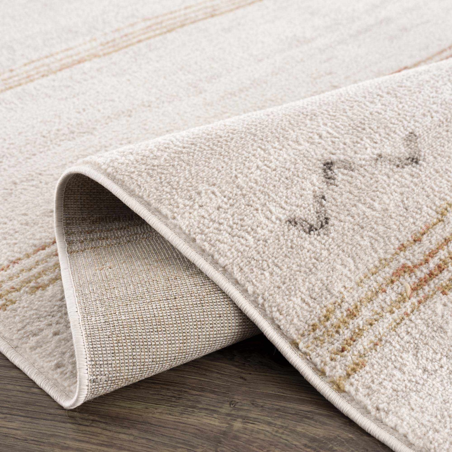 Close-up of the Deja Cream & Gold Area Rug, showing its soft pile, cream color, gold accents, and durable machine-woven construction. Fold