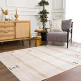 Living room scene with Deja Cream & Gold Area Rug, wood furniture, gray chair, and potted tree. Bohemian style. Roomscene-Rectangle