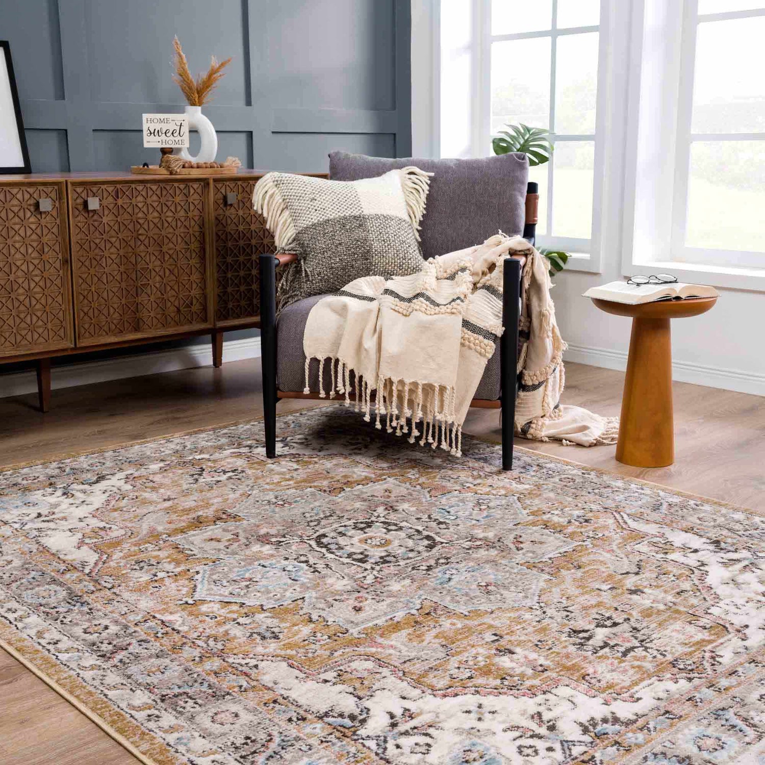 Living room scene with Albie Gold & Beige Area Rug, gray chair with throw, and wood cabinet. Neutral colors create a cozy mood. Roomscene-Rectangle