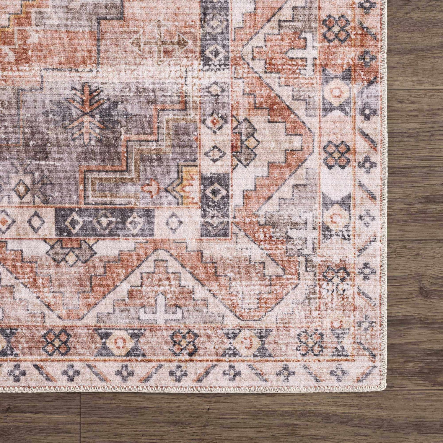 Close up of Isugod Washable Area Rug. Beige, brick red, and gray oriental rug with traditional southwestern pattern on wood floor. Swatch