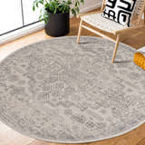 Living room scene with round Tigried Ivory & Gray area rug, wooden chair, patterned pillow, and potted plant. Roomscene-Round