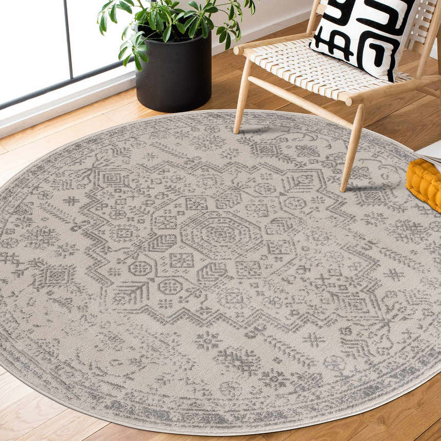 Living room scene with round Tigried Ivory & Gray area rug, wooden chair, patterned pillow, and potted plant. Roomscene-Round