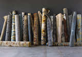 Rolled Duncansville Area Rugs in various colors and patterns against a gray wall. Rugs include traditional, farmhouse, and modern styles. Styleshot