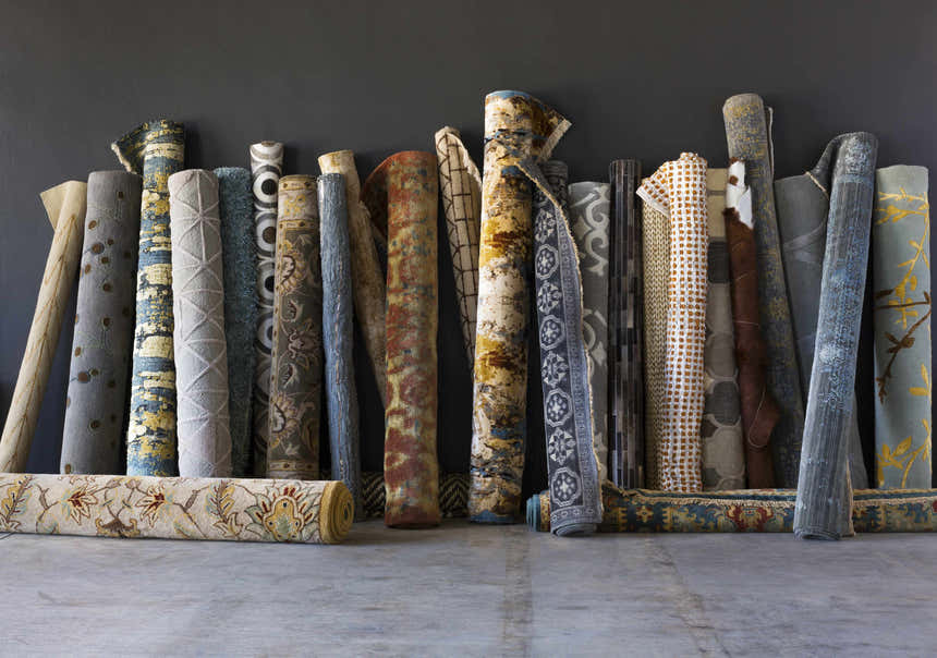 Rolled rugs on display, including a Sage Brown Elsu Area Rug with floral pattern. Styleshot