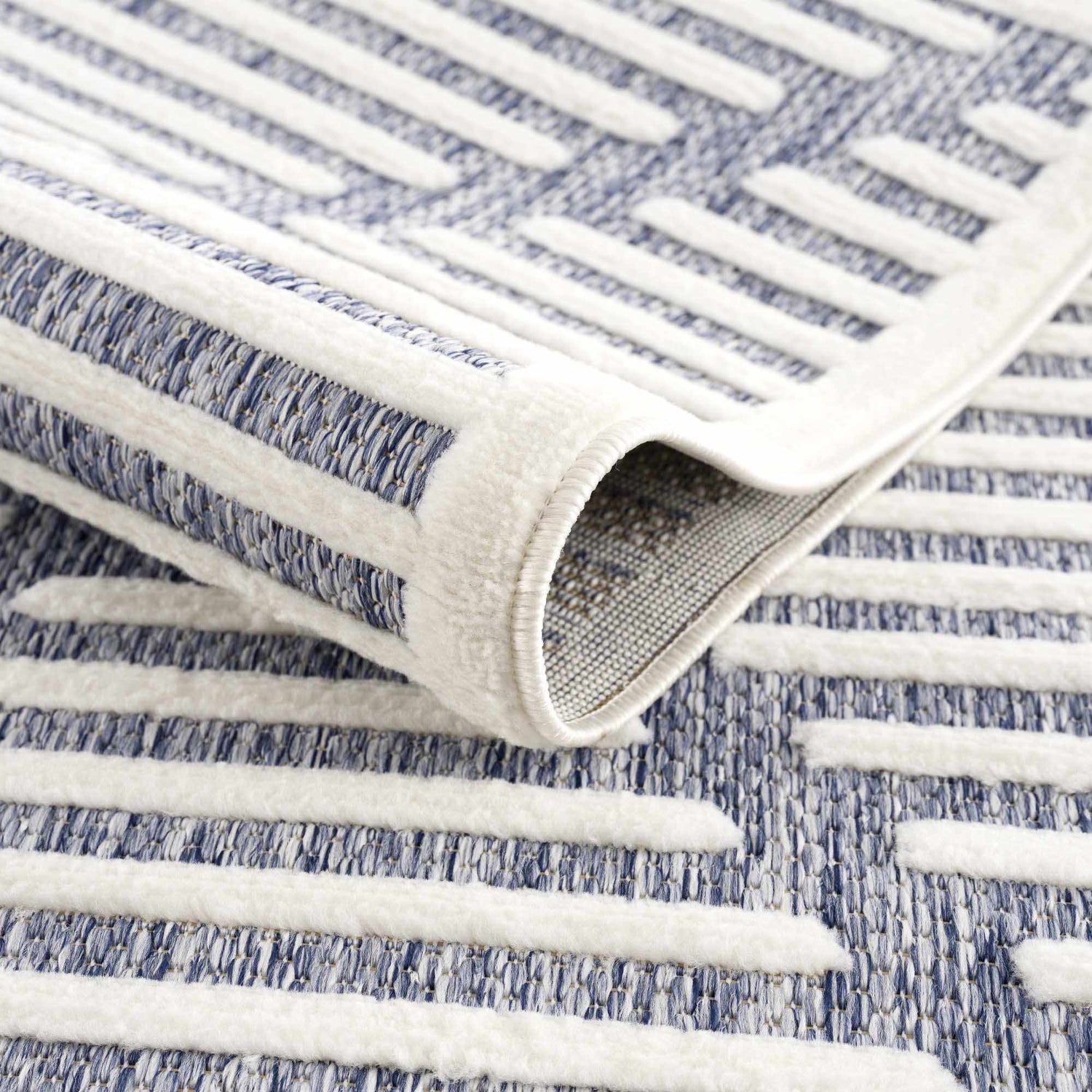 Close up of the Anah Blue Outdoor Rug featuring a contemporary geometric design and textured weave. Fold
