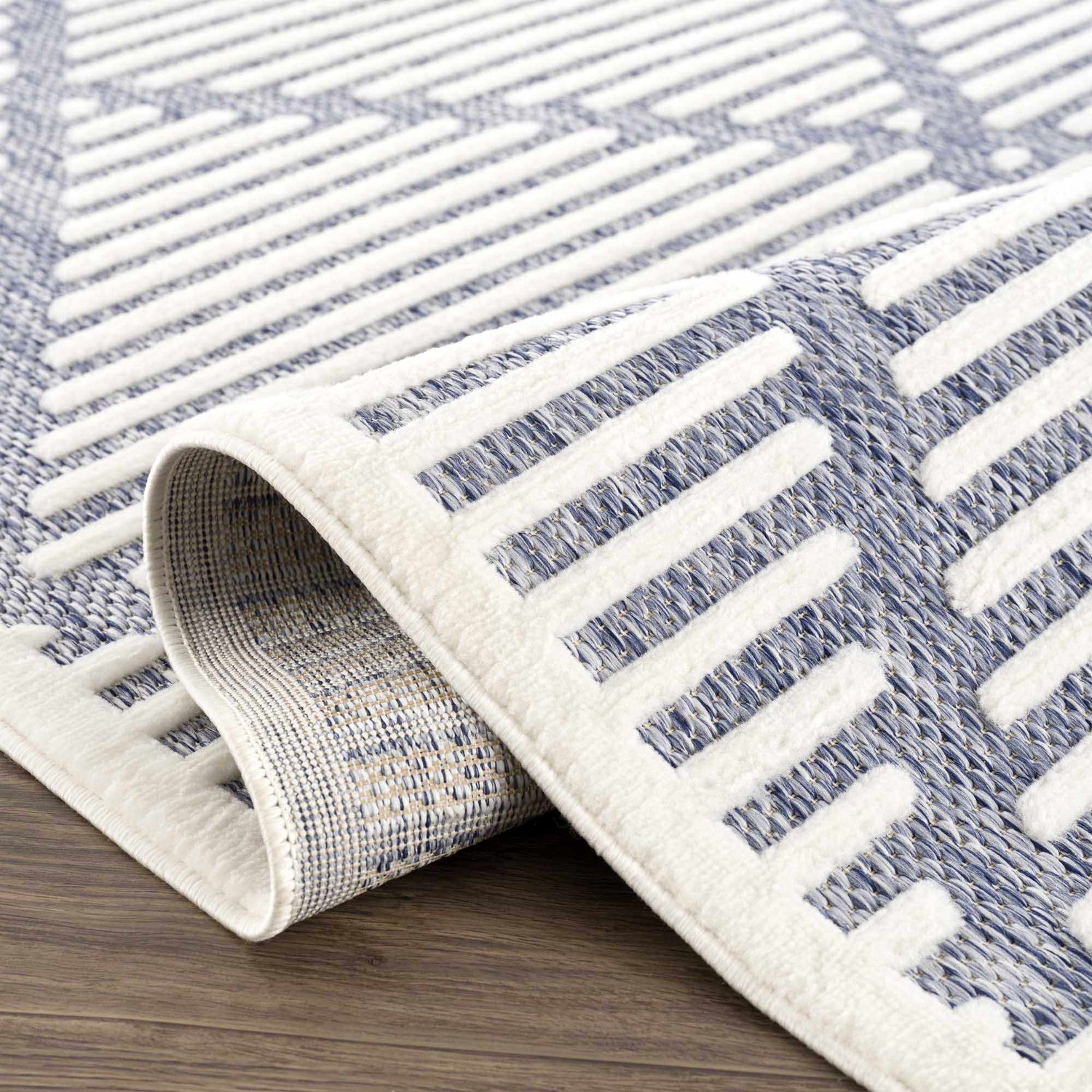 Close-up of the Anah Blue Outdoor Rug showing its geometric pattern and woven texture in denim and off-white. Fold