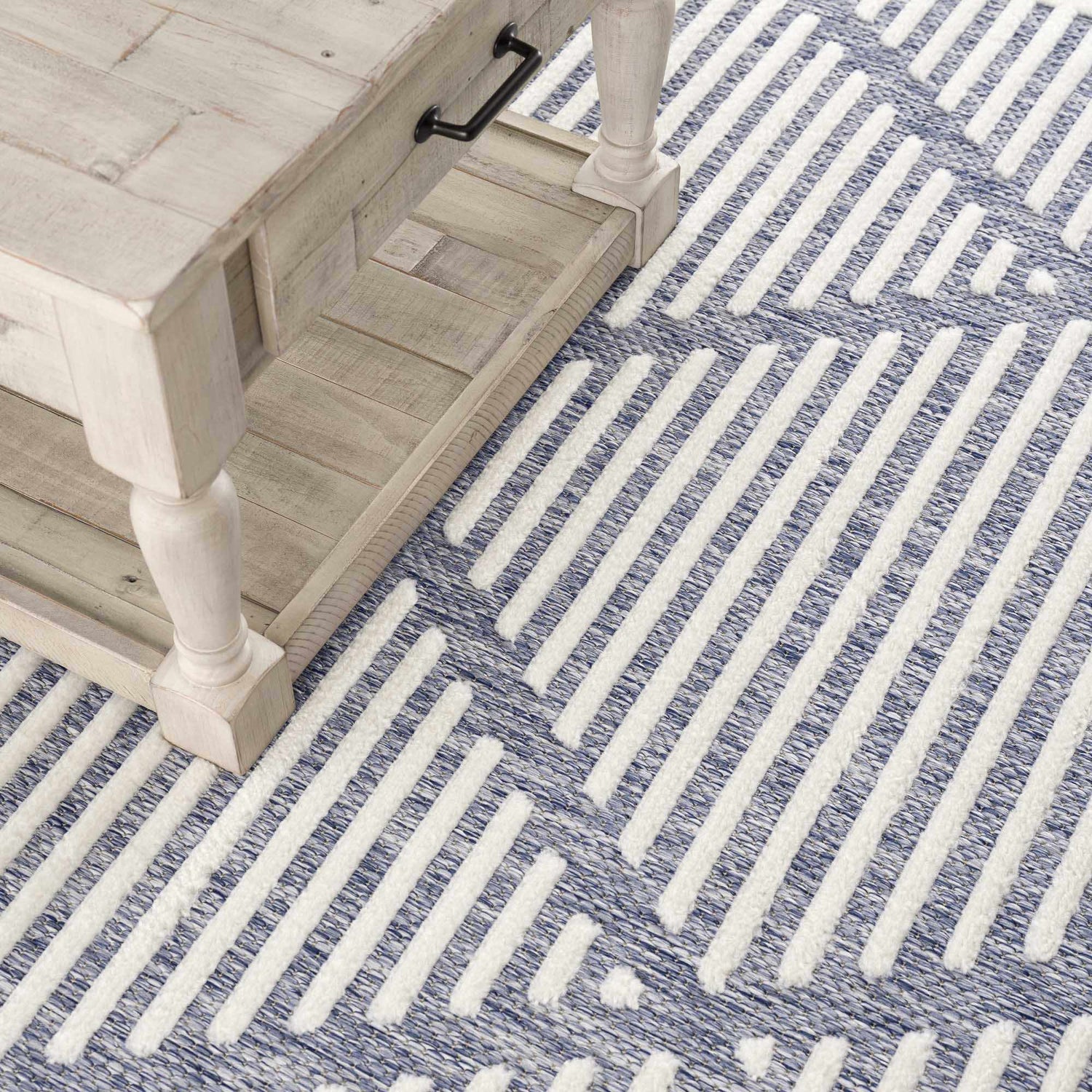 Close-up of the Anah Blue Outdoor Rug showing a white wood table and the rug's blue and white stripe pattern. Styleshot
