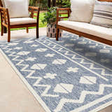 Patio scene with wooden chairs and Elio Blue Outdoor Rug featuring a geometric white pattern on a denim blue background. Roomscene-Rectangle