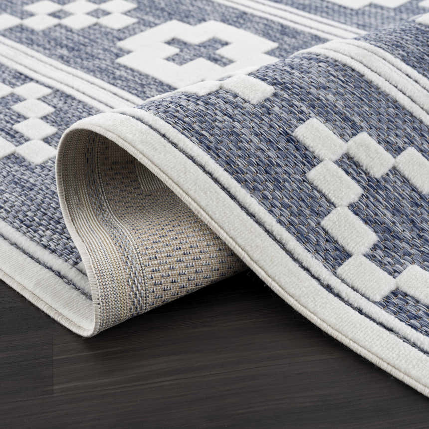 Close-up of Hiro Blue Outdoor Rug showing denim, gray, and white geometric pattern and woven texture. Fold