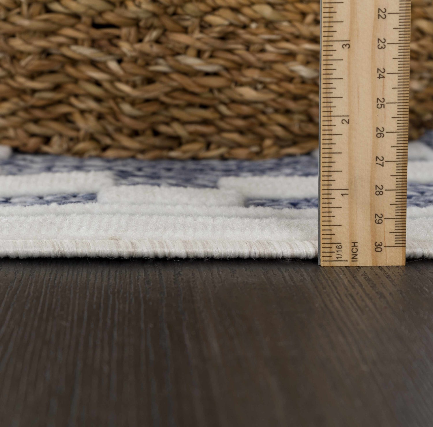 Close-up of the Hiro Blue Outdoor Rug showing pile height with a ruler and a basket on a dark wood floor. Pile