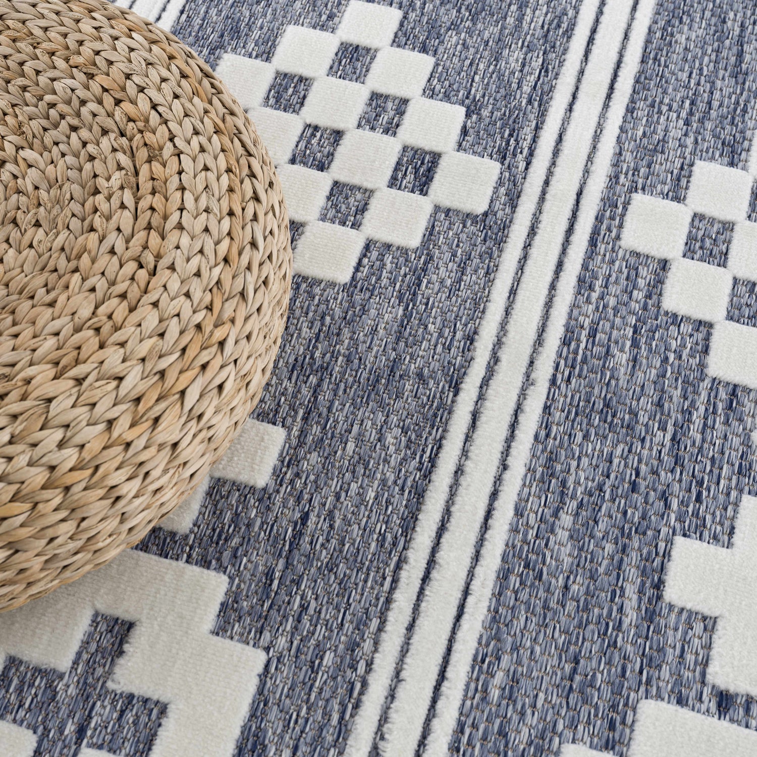 Close-up of the Hiro Blue Outdoor Rug featuring a geometric pattern and a round woven ottoman. Styleshot