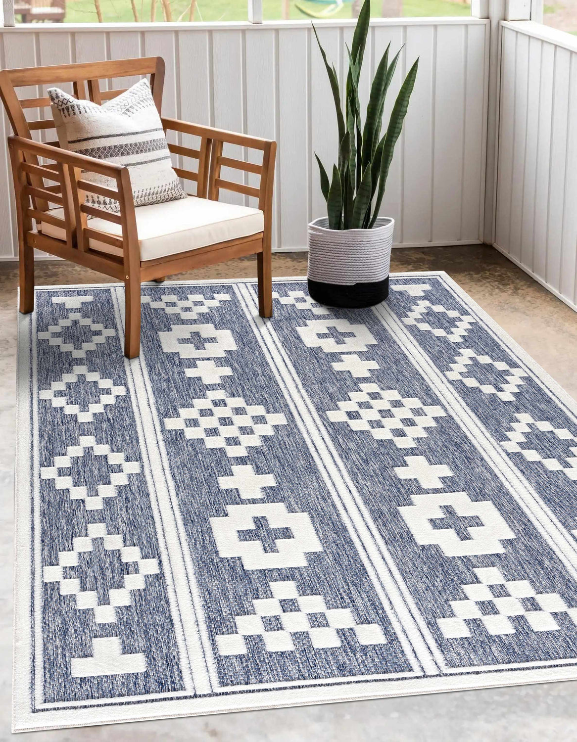 Patio scene with a Hiro Blue Outdoor Rug, wood chair, patterned pillow, and potted snake plant. Roomscene-Rectangle