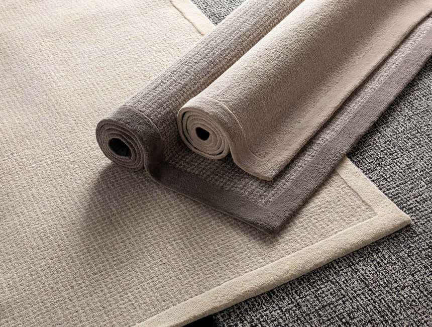 Close-up of Barrow Wool Rugs in cream and light gray, rolled to show texture and striped design. Hand-tufted wool rugs. Styleshot