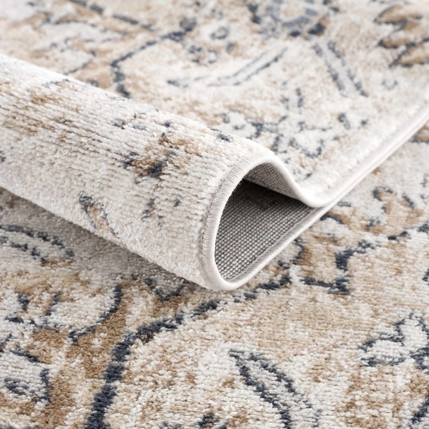 Close-up of the Mudgee Area Rug showing its charcoal, cream, beige, and tan oriental pattern and machine-woven texture. Fold