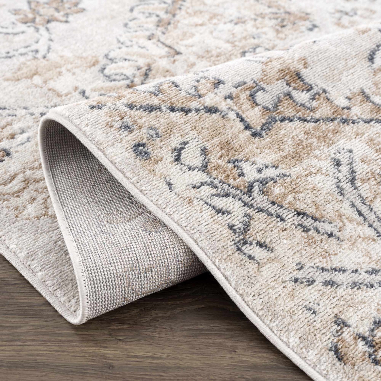 Close-up of the Mudgee Area Rug showing its charcoal, cream, beige, and tan oriental design and machine woven texture. Fold