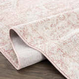 Close-up of the Snead Pink Floral Rug showing its light beige and pale pink floral pattern and machine-woven texture. Fold