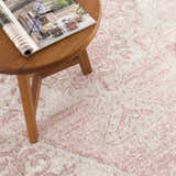 Close-up of the Snead Pink Floral Rug showing a light beige and pale pink traditional pattern with a small wood table. Styleshot