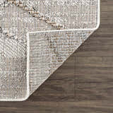 Close-up of the textured Baqer Bone & Tan Performance Rug showing its woven design and backing on a wood floor. Fold