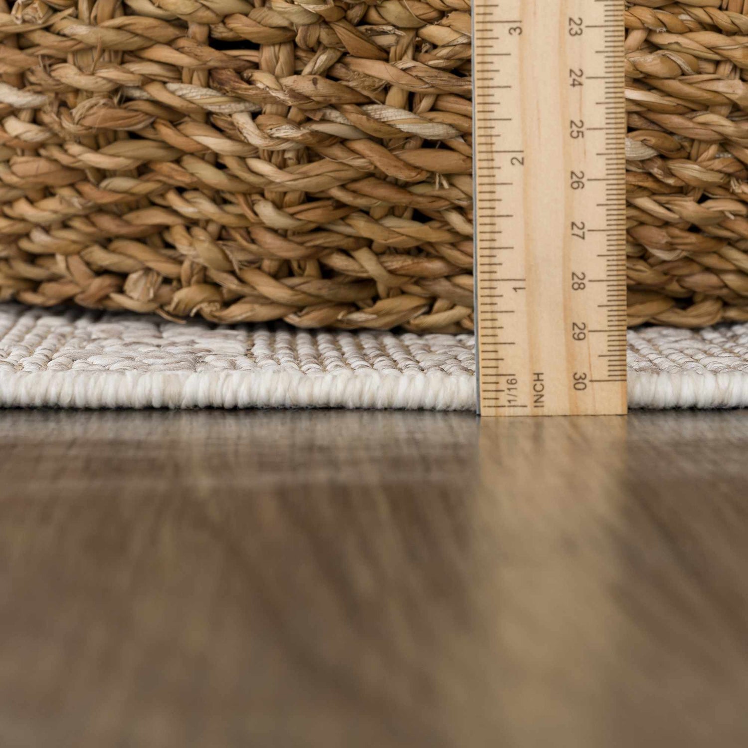 Close-up of Baqer Bone & Tan Textured Performance Rug showing pile height and texture next to a woven basket. Pile