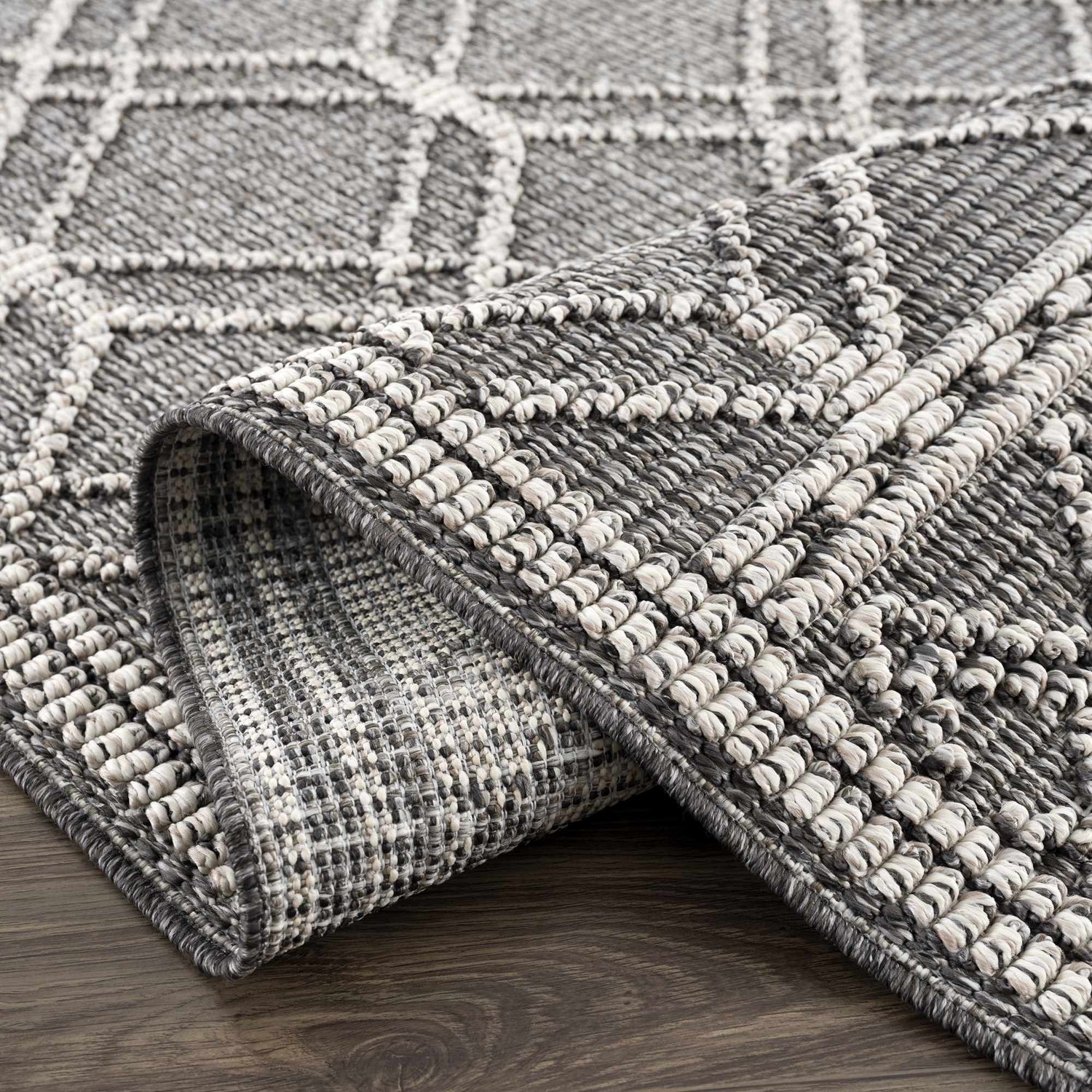 Close-up of the Diah Black & Bone Area Rug showing its geometric pattern and textured, machine-woven construction. Fold