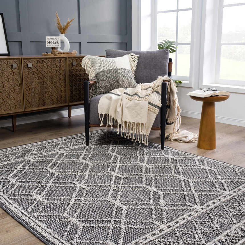 Living room scene with a Diah Black & Bone Area Rug, gray chair, wood cabinet, and neutral decor. Roomscene-Rectangle