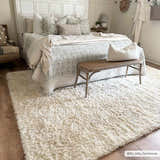 Bedroom scene with a cream Siari Solid Plush Rug, white bedding, and a wooden bench for a cozy, neutral aesthetic. Roomscene-Rectangle