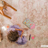 Child playing on a Snead Pink Floral Rug in a kids room with a wooden rocking horse. Styleshot