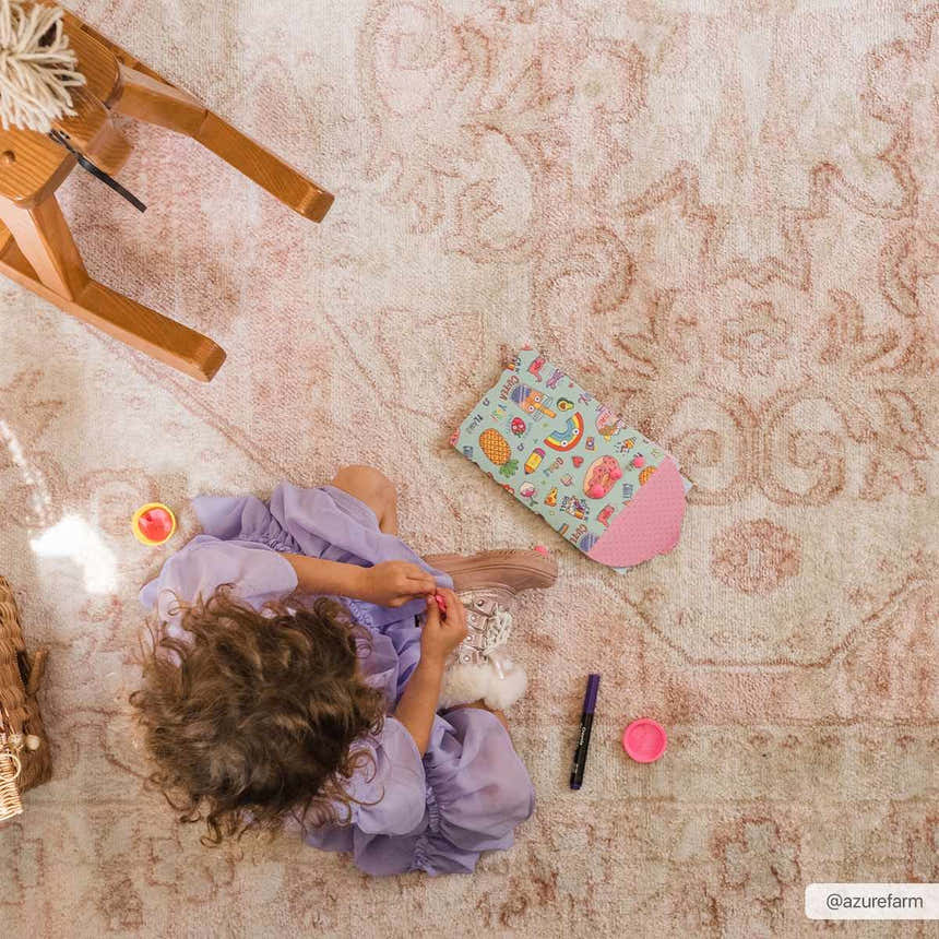 Child playing on a Snead Pink Floral Rug in a kids room with a wooden rocking horse. Styleshot