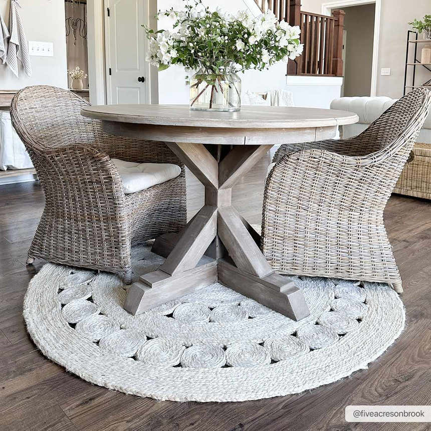 Farmhouse dining room with a Stafford Bleached Jute Round Rug under a wood table and wicker chairs. Roomscene-Round