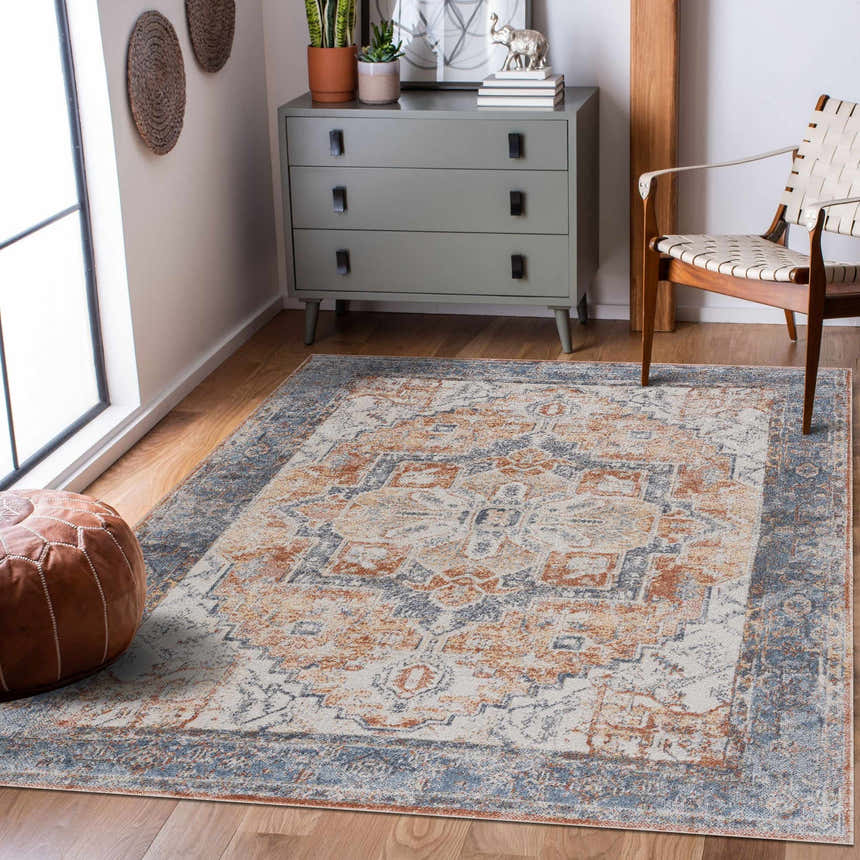 Living room scene with Blue Orange Hera Washable rug, gray dresser, leather pouf, and woven chair on wood floor. Roomscene-Rectangle