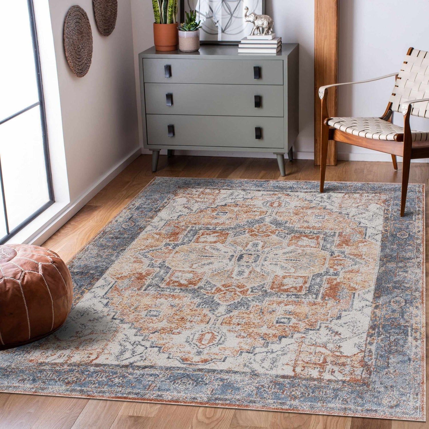 Living room scene with Blue Orange Hera Washable rug, gray dresser, leather pouf, and woven chair on wood floor. Roomscene-Rectangle