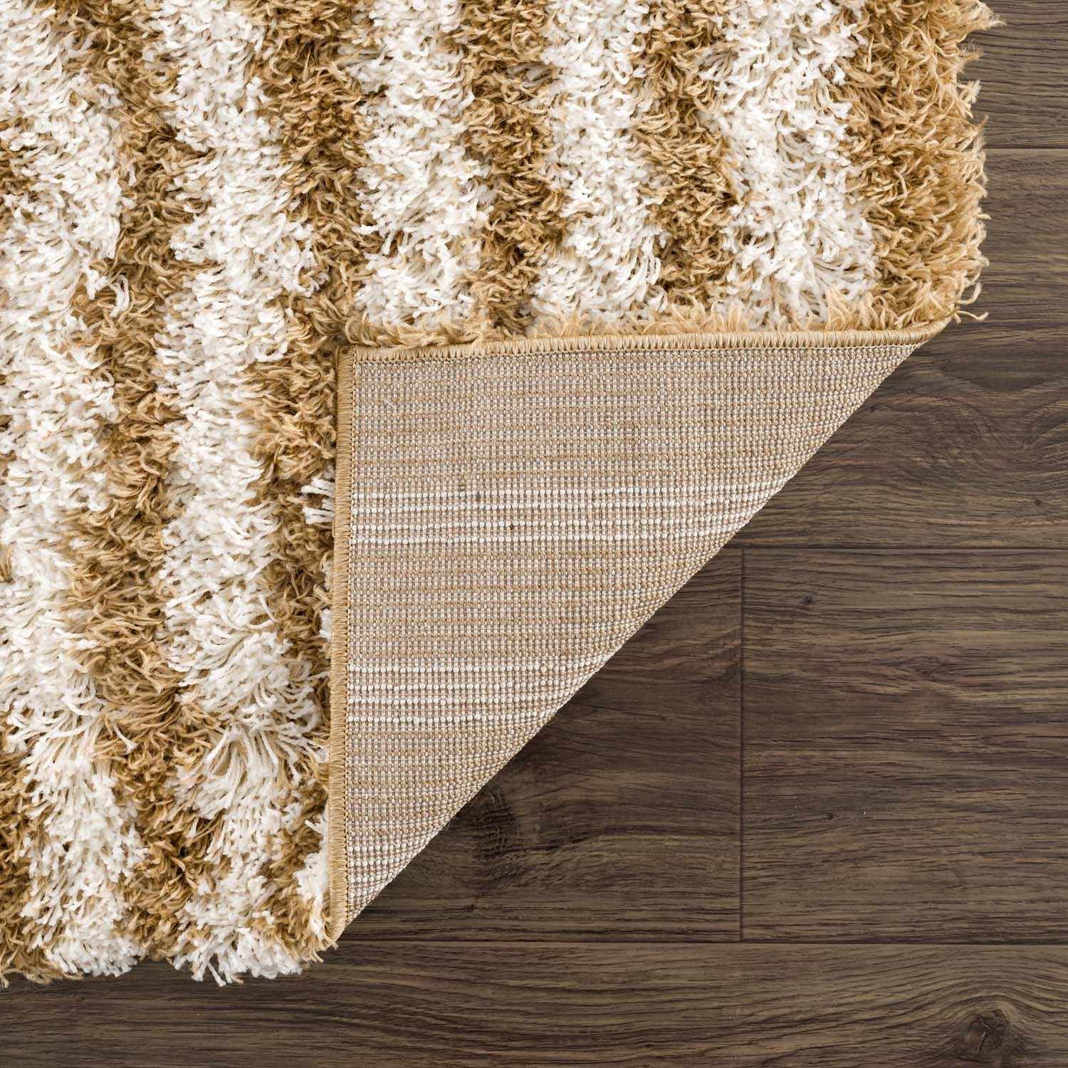 Close-up of the Calup Shag Area Rug showing bone and dark brown shaggy texture and backing on dark wood floors. Fold